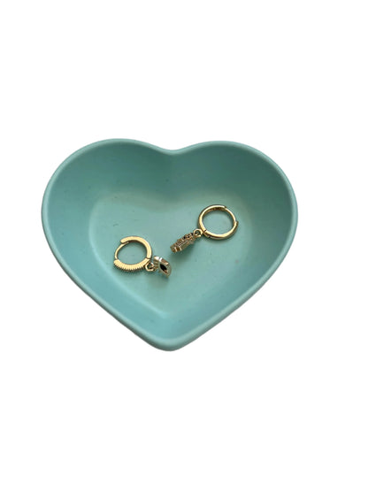 A pair of gold hoop earrings with a small charm, displayed inside a light blue heart-shaped ceramic tray on a white background.