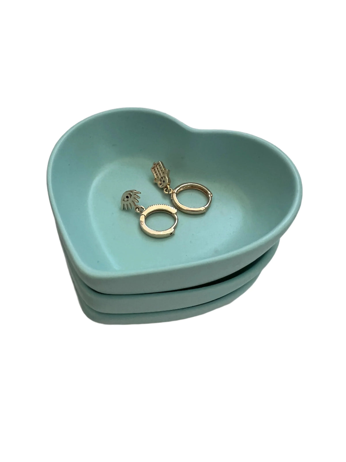 A pair of gold huggie hoop earrings with a small textured drop charm, displayed inside a light blue heart-shaped ceramic jewelry tray on a white background.