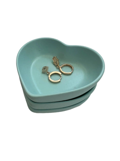 A pair of gold huggie hoop earrings with a small textured drop charm, displayed inside a light blue heart-shaped ceramic jewelry tray on a white background.