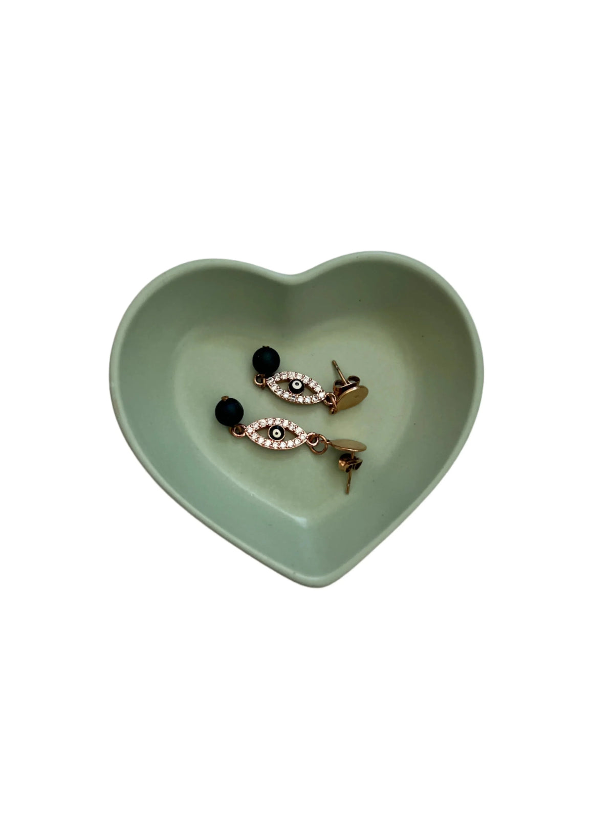 A pair of gold-toned statement earrings with black round beads and white rhinestone-encrusted teardrop details, displayed inside a small mint green heart-shaped dish on a white background.