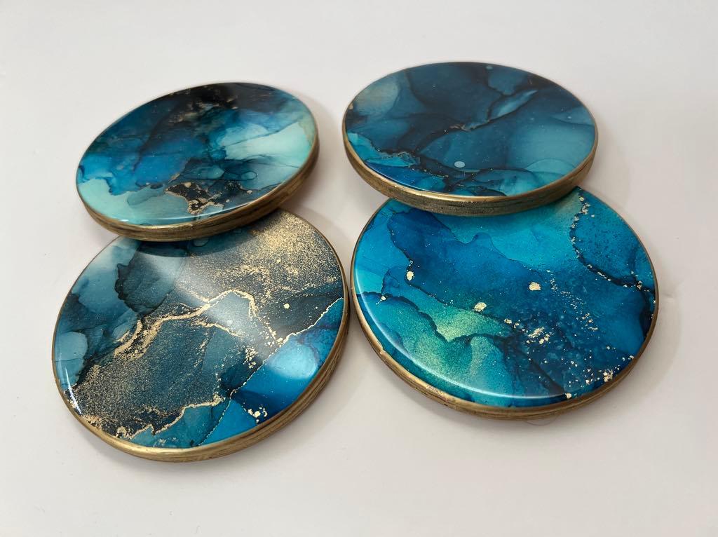 Four round abstract resin coasters with blue and teal alcohol ink design and gold metallic edges